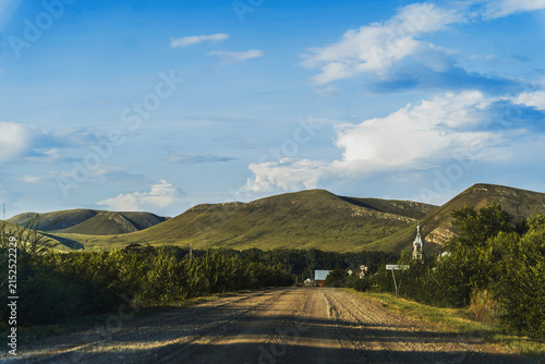 Obraz na płótnie Rustic dirt road leading to rolling green hills under a bright blue sky