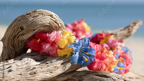 Bright Hawaiian lei made of colorful flowers rests on weathered driftwood along sunny tropical beach.