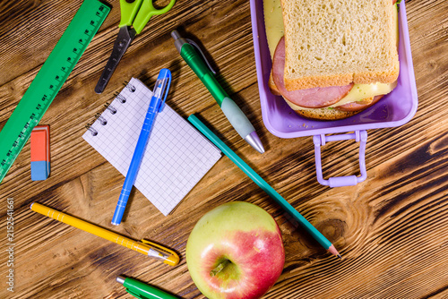 Ripe apple, different stationeries and lunch box with sandwiches on a wooden table. Top view