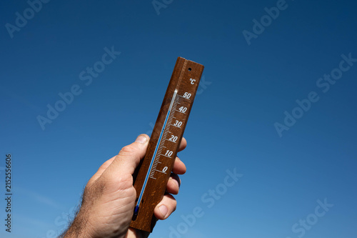 Hand holding wooden outdoor thermometer against clear blue sky showing summer heat