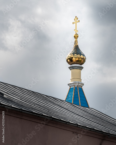 Canvastavla Golden onion dome with an Orthodox cross rising above a church roof against a dramatic cloudy sky, highlighting traditional Eastern Orthodox religious architecture
