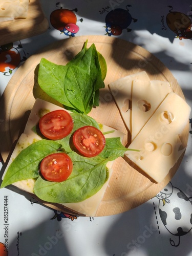 Fresh tomato slices, cheese and spinach leaves on a wooden board at a countryside veranda, healthy summer snack