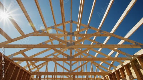 New Home Construction: Wooden Roof Trusses and Framing Against Blue Sky with Sun Flare, ideal for real estate and building industry projects.