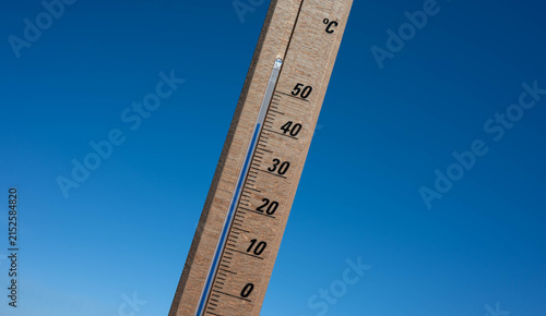 Wooden thermometer showing high summer temperature against clear blue sky