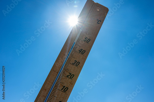 Wooden thermometer showing high summer temperature against clear blue sky