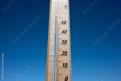 Wooden thermometer showing high summer temperature against clear blue sky