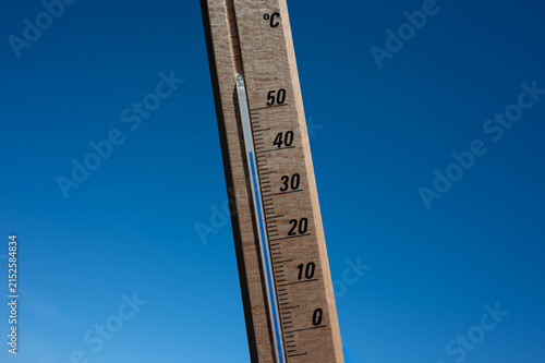 Wooden thermometer showing high summer temperature against clear blue sky