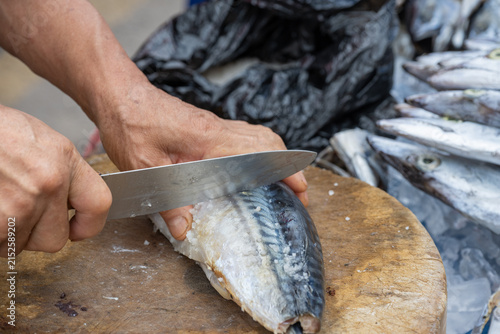 Fotografie A vendor cuts salted mackerel with a kitchen knife on a wooden chopping block at a traditional Korean street market