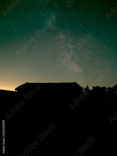 Quadro su tela Voie lactée traversant un ciel étoilé d’été au-dessus de la silhouette sombre d’une maison et de la végétation à la campagne, paysage nocturne photographié en Bretagne au mois d'août