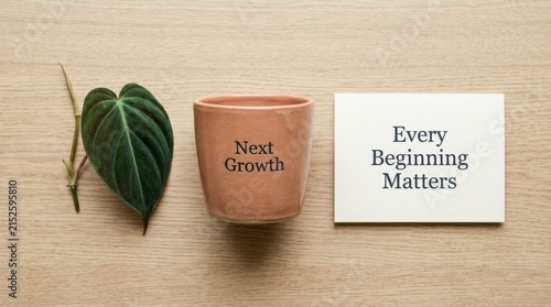 Inspiring flat lay featuring a small terracotta pot labeled Next Growth alongside a vibrant green philodendron leaf and a card stating Every Beginning Matters on a neutral light wood