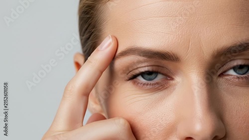 Close up of a womans face with her finger on her temple, showing her eye and forehead.