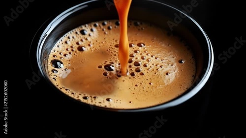 Rich espresso coffee pouring into black cup with frothy crema and bubbles in dark setting