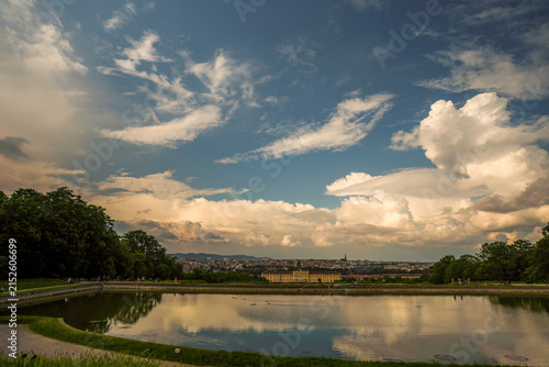 Scenic view of Schönbrunn Palace across the pond in Vienna, Austria, with dramatic clouds and manicured gardens. Perfect for travel and architecture concepts.