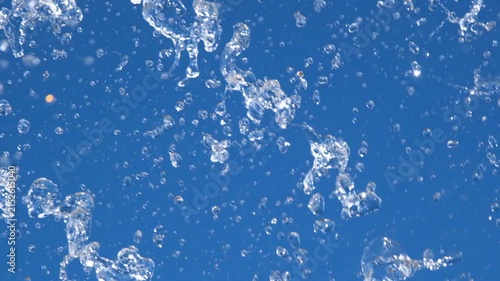Close-up of sparkling fountain water splashes against clear blue sky. Refreshing droplets create dynamic abstract background representing freshness, summer, energy and motion