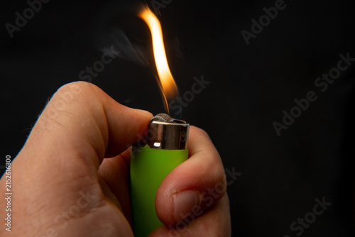 Hand holding a burning green lighter on a black background.