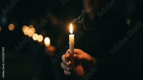 Close up of a hand holding a glowing candle during a peaceful night vigil in the dark, symbolizing hope and remembrance for a memorial service, perfect for spiritual and religious themes or mourning