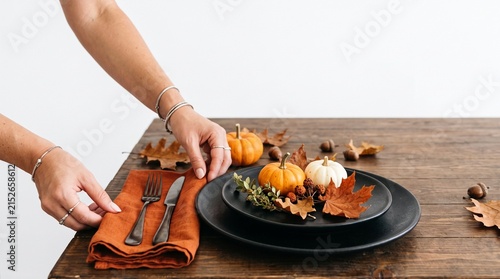 Person setting a table with pumpkins and autumn leaves for a festive fall harvest meal