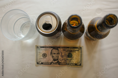 Top View of Beer Bottles Can Glass and Five Dollar Bill on White Table