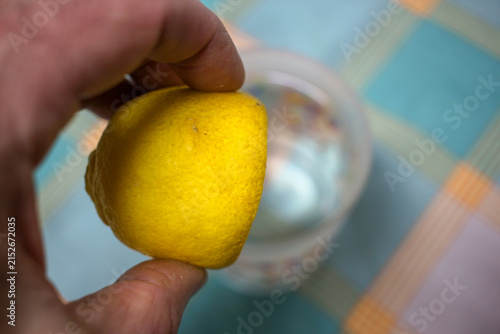 Close Up of Hand Squeezing Lemon Half Into Glass Below