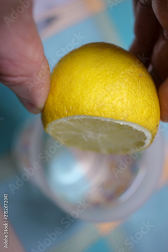 Hand Squeezing Fresh Yellow Lemon Half Over Glass Table