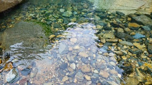 Clear shallow water flowing over rocky stream bed with pebbles and stones.
