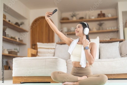 Asian woman taking fitness selfie with smartphone after home workout. Happy active lifestyle, post workout relaxation, social media content creator, health wellness and daily physical activities
