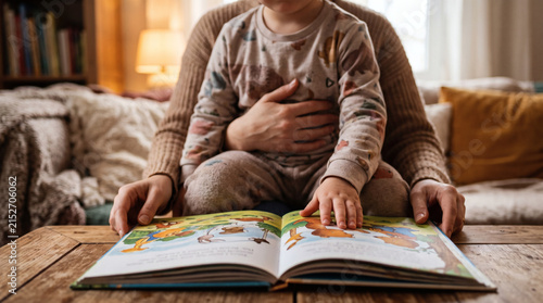Close up of a child sitting on parent lap reading a picture book together at home
