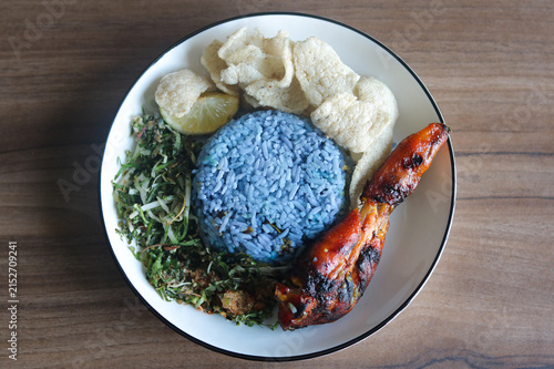 Принти на полотні Top-down view of a plate of Malaysian Nasi Kerabu featuring blue pea flower rice served with grilled chicken, raw vegetable and herb salad (ulam), and fish crackers