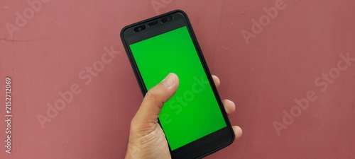 Hand holding a smartphone with a green screen background.