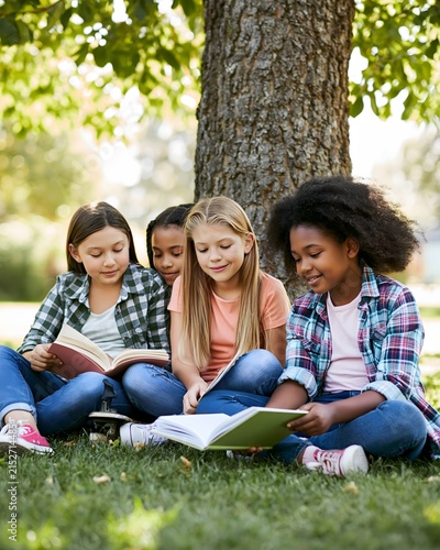 Diverse girls reading books together beneath a large tree in a peaceful school garden, literacy education, friendship, knowledge and equal opportunities, warm afternoon sunlight, natural expressions,