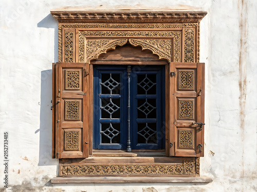 Indian heritage window with octagonal geometric design, finely carved wooden frame, antique brass hardware, deep navy shutters, weathered traditional wall