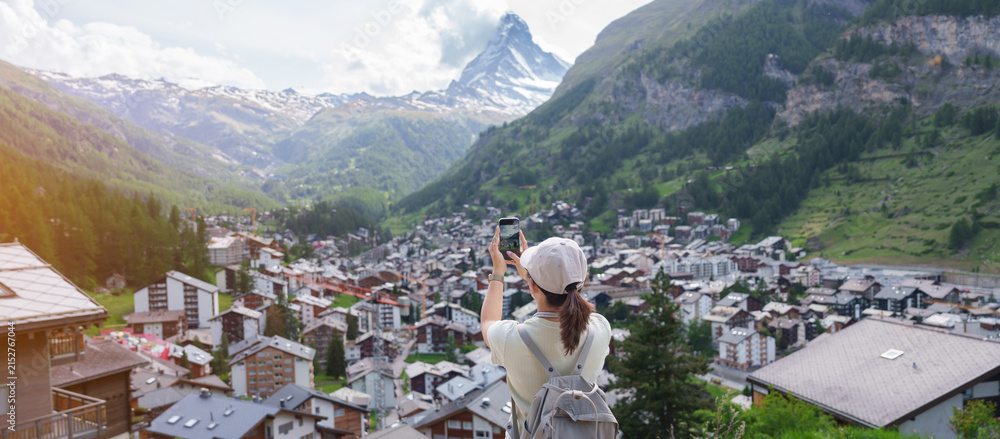 Fototapeta premium Woman Tourist Exploring Zermatt, Switzerland. Happy Traveler Taking Photo with Smartphone at Zermatt Village Viewpoint and Matterhorn. Popular Tourist Attraction and Travel Destination in Europe