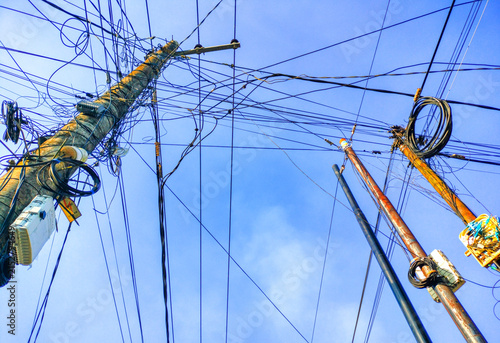 Tangled utility poles and messy overhead power lines against blue sky