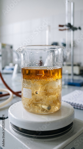 Laboratory beaker with golden liquid sample placed on magnetic stirrer hotplate