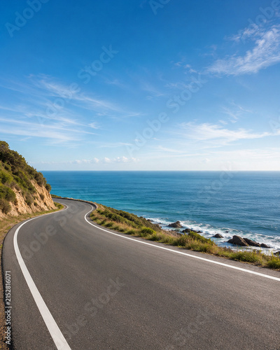 Scenic winding coastal road along the ocean with a clear blue sky, ideal for automotive commercial promotion and vehicle display mockup.
