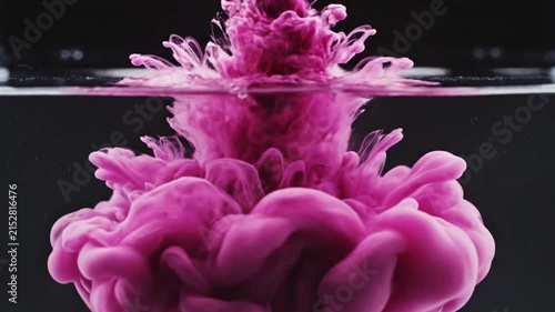 Pink ink drop spreading in dark water background.