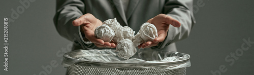 Frustration and Failure: A person in business attire holds crumpled paper balls, symbolizing failed ideas or efforts, as they are about to discard them into a waste bin.