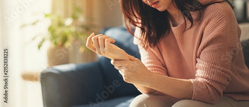 Woman massaging painful wrist from joint inflammation while sitting on cozy living room sofa