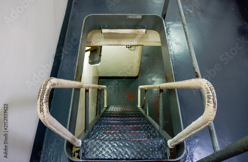 Interior Steel Hatch Companionway Ladder on Military Warship. High angle view looking down narrow steel companionway ladder with wrapped handrails leading to lower deck compartment inside naval vessel