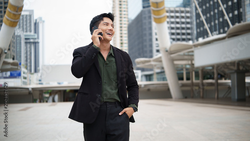Asian businessman talking on a smartphone while standing in a modern city district.