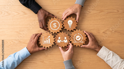 Diverse hands connecting wooden gears with business icons on a table. Concept of teamwork, strategy, financial growth, and partnership