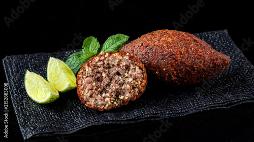A crispy, fried meat kibbeh sits on a black paper towel against a black background