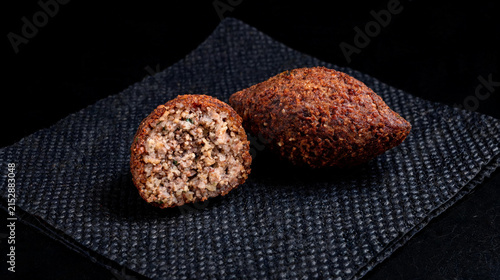 A crispy, fried meat kibbeh sits on a black paper towel against a black background