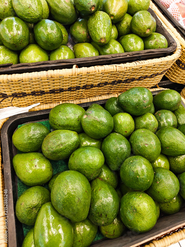 Fresh avocados fill woven baskets. They rest on a market stall. Green skins gleam under natural light. Their round shapes and slight curves appeal. Farmers may sell them for daily use