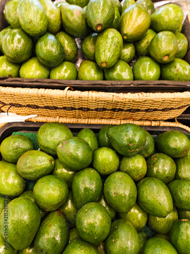 Fresh avocados fill woven baskets. They rest on a market stall. Green skins gleam under natural light. Their round shapes and slight curves appeal. Farmers may sell them for daily use