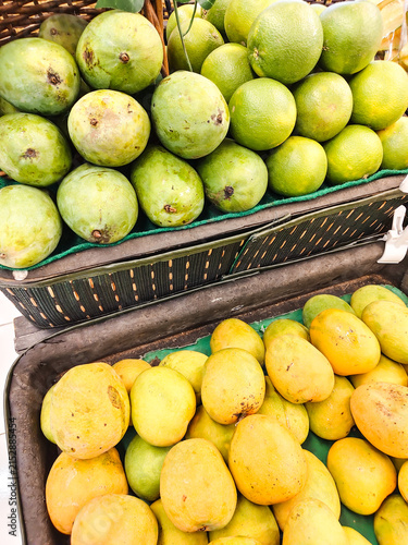 Fresh mangoes and lemons display vibrant colors. Bright yellow lemons sit beside green mangoes. Baskets hold fruit in a market stall. Natural sunlight highlights each fruit's texture