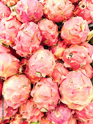 Bright pink dragon fruits pile high in woven baskets. Their scales glisten under warm market lighting. Vibrant colors draw attention to fresh, exotic produce. Ideal for food, health. No people present