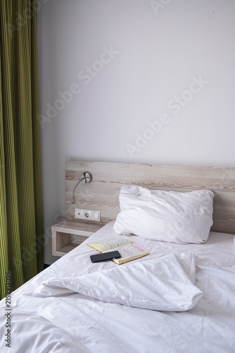 A smart phone and a note book on a neatly made hotel bed, symbolizing a peaceful morning routine.