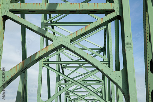 Close up of green steel truss structure of a bridge against a blue sky