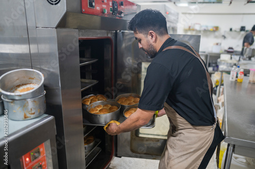 Foto Latino baker putting fresh bread into commercial oven